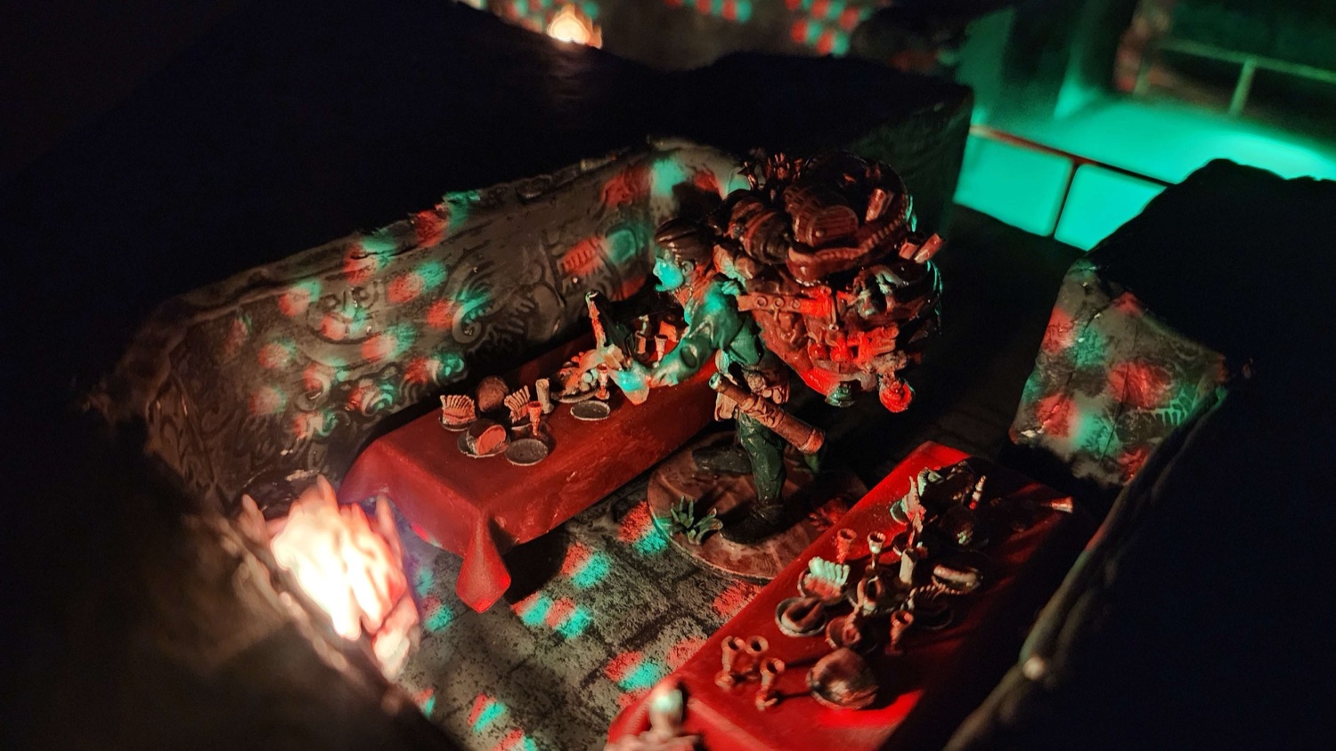 A torch-lit alcove containing painted miniatures around a table.